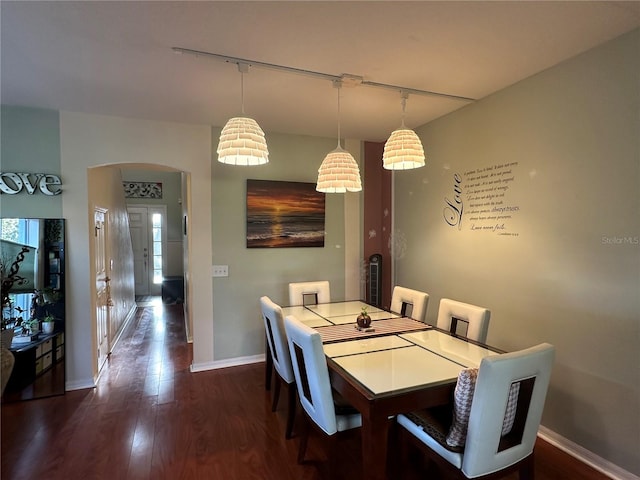 dining area with dark wood-type flooring and track lighting