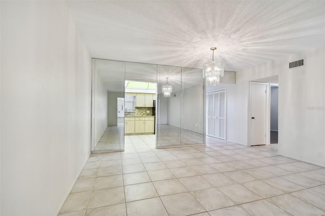 unfurnished room with light tile patterned flooring, a textured ceiling, and an inviting chandelier