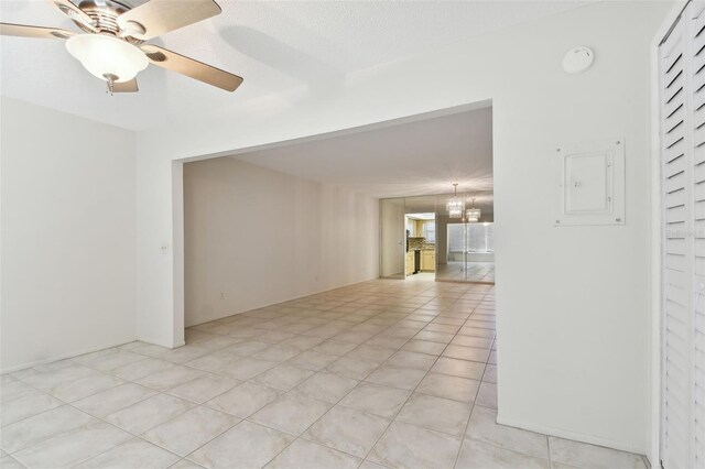 tiled spare room with ceiling fan with notable chandelier and electric panel