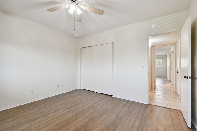 unfurnished bedroom featuring ceiling fan, a closet, light hardwood / wood-style floors, and a textured ceiling