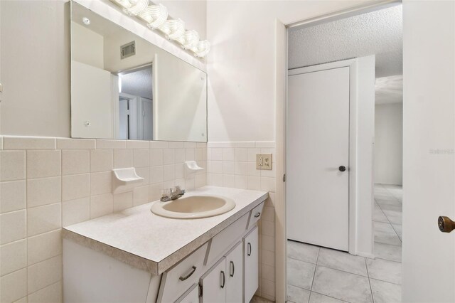 bathroom with tile patterned floors, vanity, tile walls, and a textured ceiling