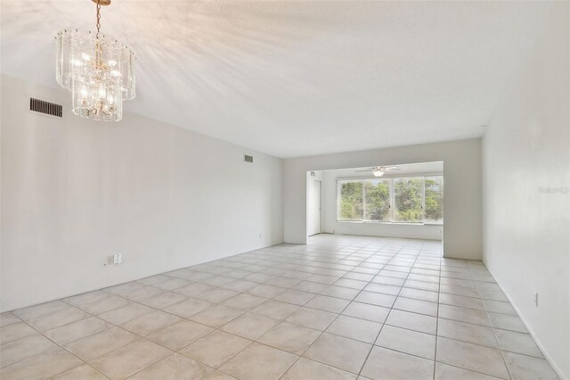 tiled spare room with ceiling fan with notable chandelier