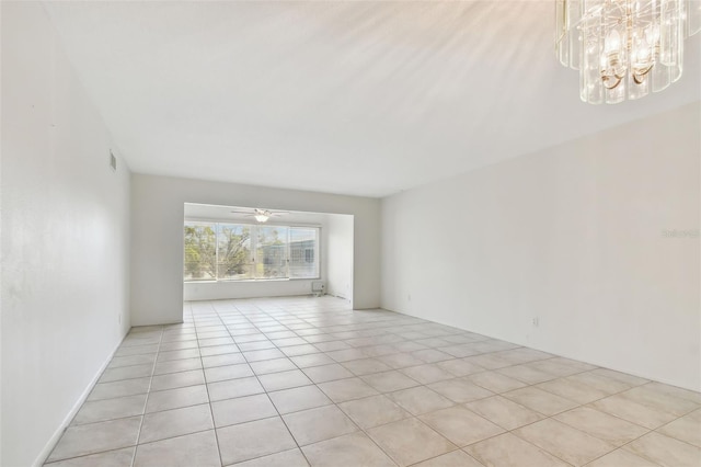 tiled empty room with ceiling fan with notable chandelier