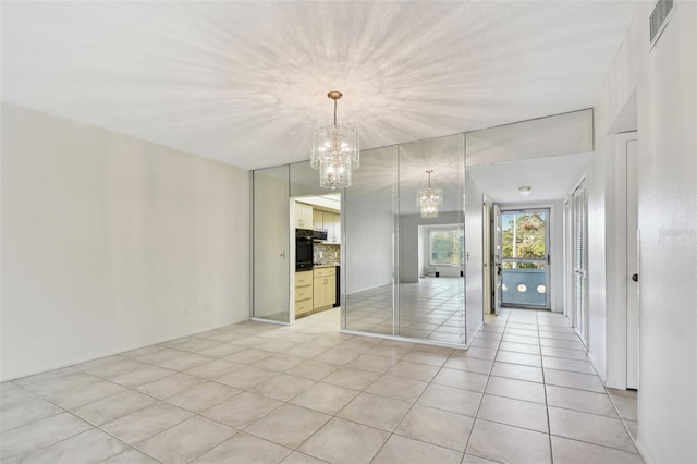 tiled spare room with a notable chandelier