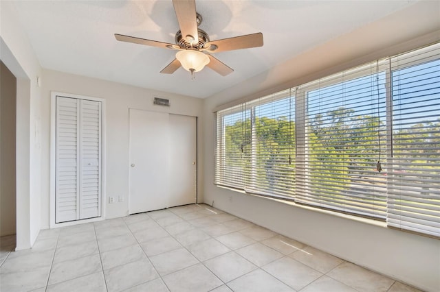 unfurnished bedroom featuring light tile patterned floors, ceiling fan, and multiple closets