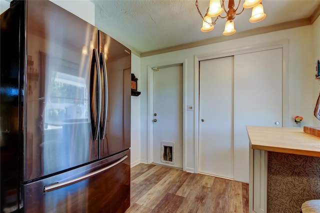 kitchen with an inviting chandelier, ornamental molding, butcher block countertops, light hardwood / wood-style floors, and stainless steel refrigerator