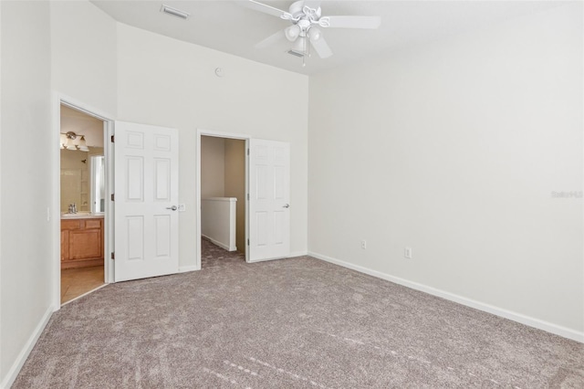 unfurnished bedroom with carpet, ensuite bathroom, ceiling fan, and a towering ceiling