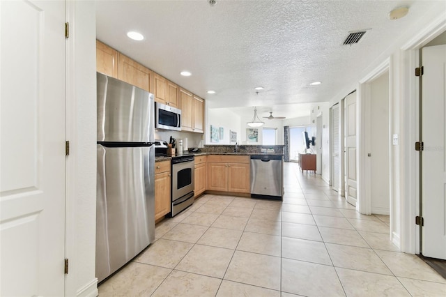 kitchen with pendant lighting, a textured ceiling, light brown cabinetry, light tile patterned floors, and appliances with stainless steel finishes