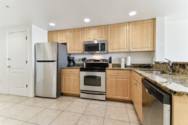 kitchen with light brown cabinets, dark stone countertops, a textured ceiling, appliances with stainless steel finishes, and light tile patterned flooring