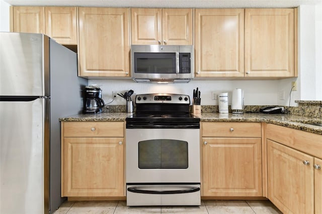 kitchen with light brown cabinets, dark stone countertops, light tile patterned floors, and stainless steel appliances