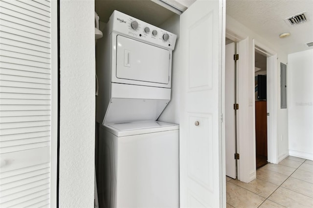 laundry room with light tile patterned floors, a textured ceiling, and stacked washer / dryer