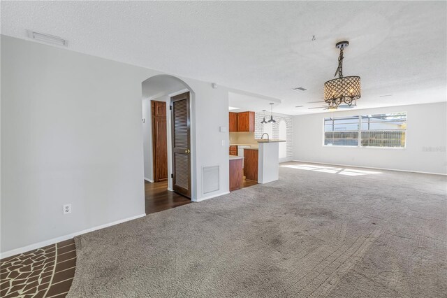 unfurnished living room featuring sink, a textured ceiling, and dark colored carpet