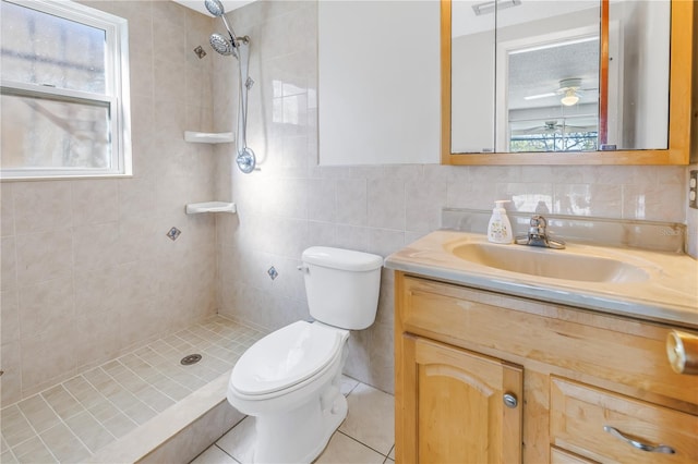 bathroom featuring tile walls, vanity, tiled shower, ceiling fan, and toilet