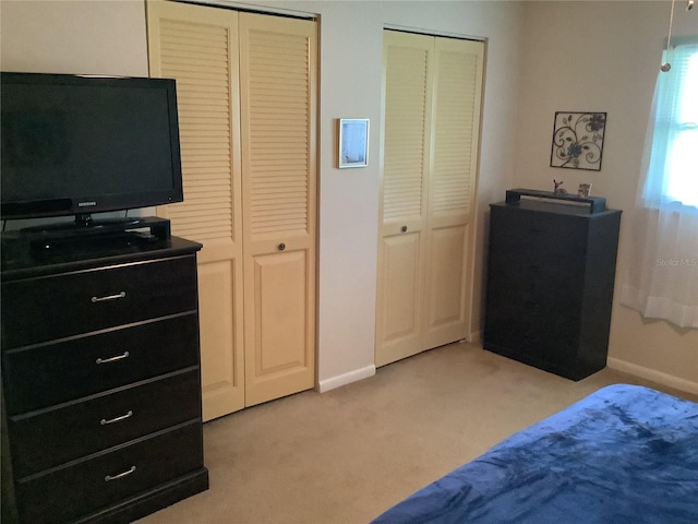 bedroom with light colored carpet and two closets