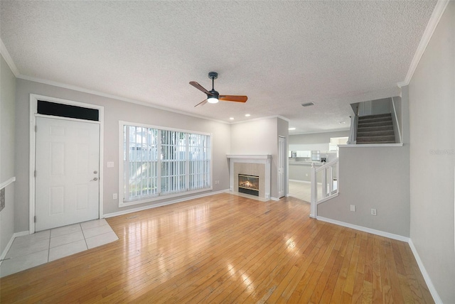 unfurnished living room with ceiling fan, ornamental molding, a textured ceiling, and light hardwood / wood-style flooring