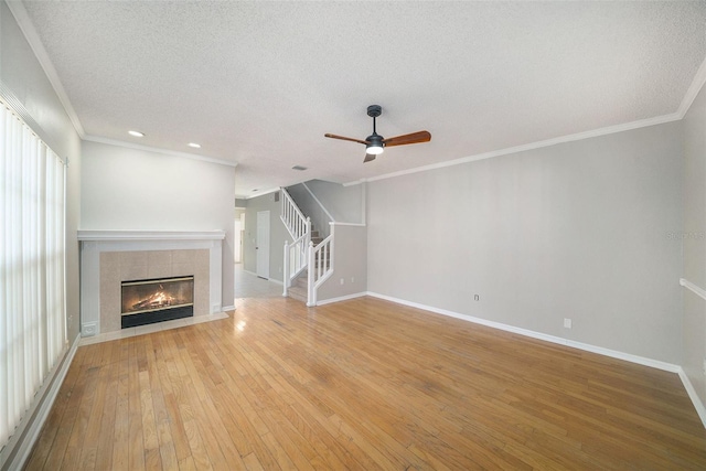 unfurnished living room featuring a tile fireplace, light hardwood / wood-style flooring, ceiling fan, ornamental molding, and a textured ceiling