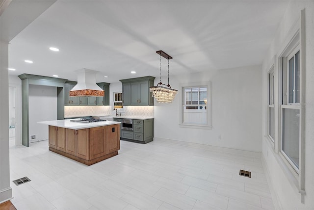 kitchen featuring premium range hood, a kitchen island, tasteful backsplash, hanging light fixtures, and stainless steel gas cooktop