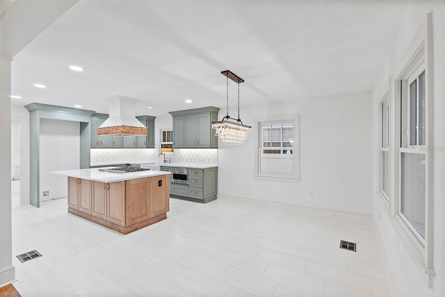 kitchen featuring pendant lighting, premium range hood, stainless steel gas cooktop, a kitchen island, and decorative backsplash