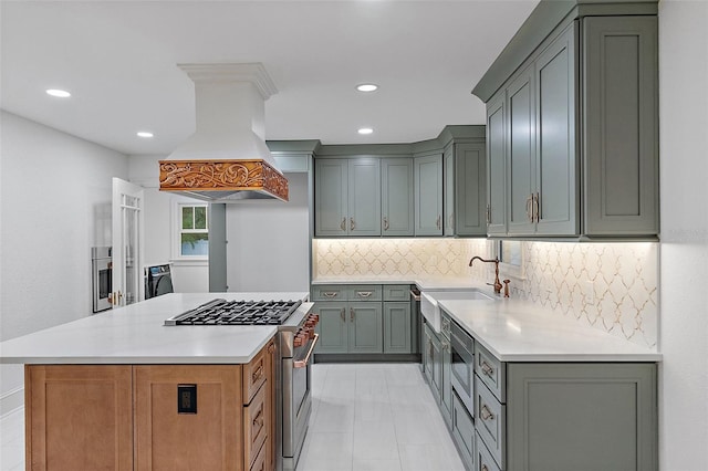 kitchen with a kitchen island, appliances with stainless steel finishes, tasteful backsplash, sink, and custom range hood