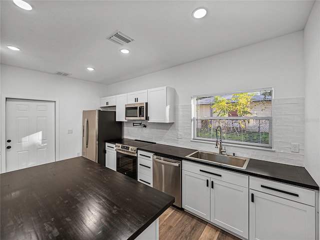 kitchen with appliances with stainless steel finishes, tasteful backsplash, dark wood-type flooring, sink, and white cabinets