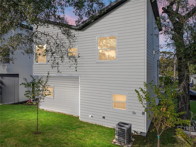 property exterior at dusk with a lawn and central AC unit