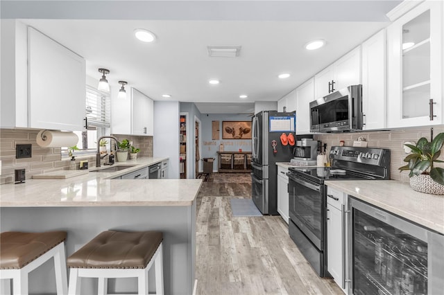 kitchen featuring appliances with stainless steel finishes, white cabinetry, kitchen peninsula, a breakfast bar area, and beverage cooler