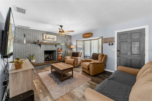 living room with a fireplace, a textured ceiling, ceiling fan, and dark wood-type flooring