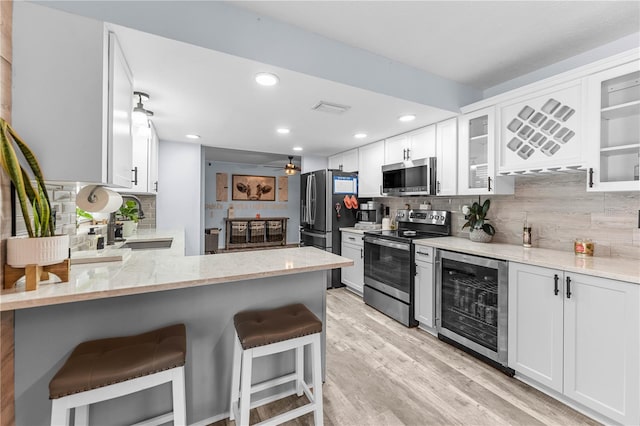 kitchen featuring a kitchen bar, light wood-type flooring, stainless steel appliances, white cabinetry, and wine cooler