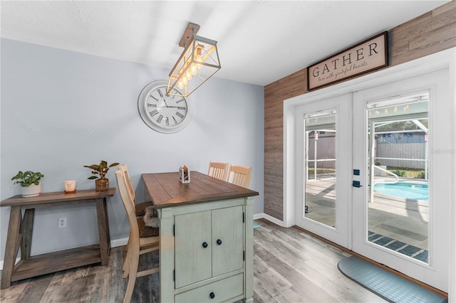 dining space with french doors, light wood-type flooring, and wood walls