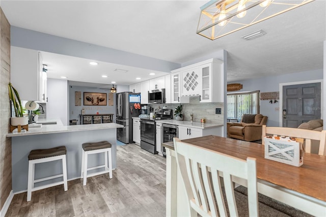 kitchen with a breakfast bar, kitchen peninsula, appliances with stainless steel finishes, light hardwood / wood-style floors, and white cabinetry