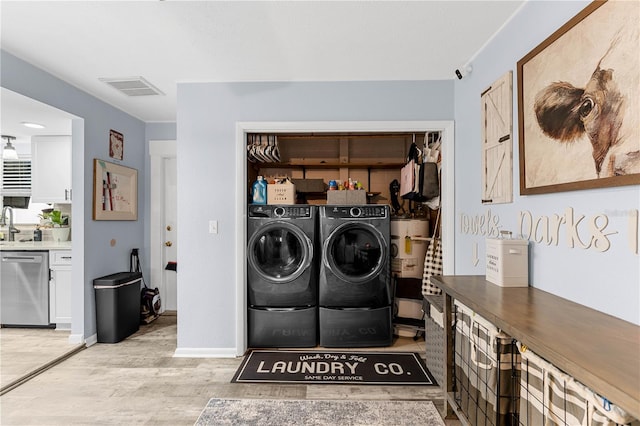 laundry area with washing machine and dryer, gas water heater, and light hardwood / wood-style flooring