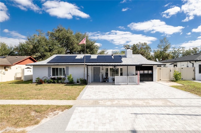 ranch-style home featuring solar panels, covered porch, and a front yard