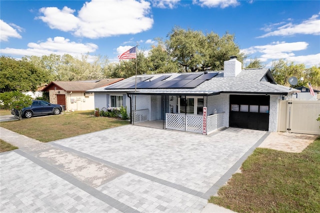 ranch-style house featuring a front yard, solar panels, a garage, and covered porch