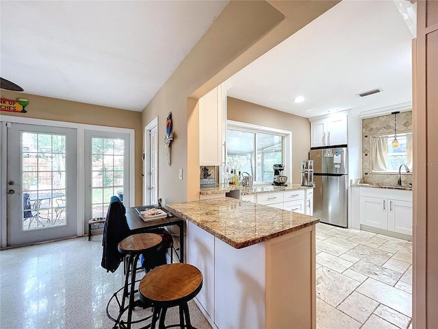 kitchen featuring kitchen peninsula, a kitchen breakfast bar, light stone countertops, white cabinets, and stainless steel refrigerator