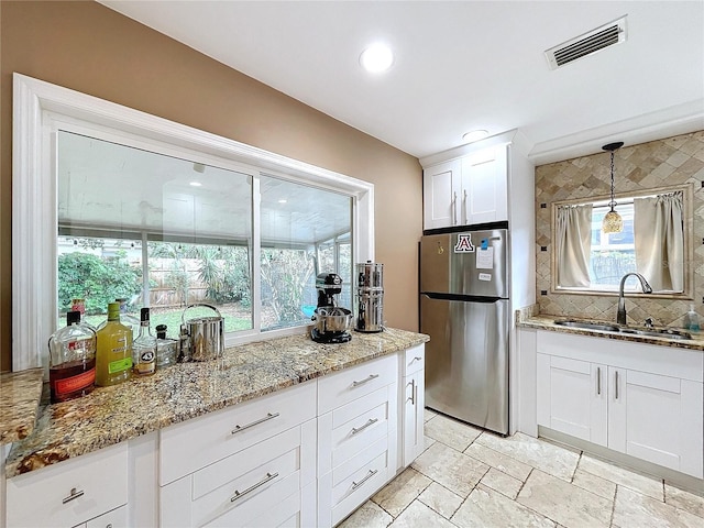 kitchen featuring pendant lighting, white cabinets, sink, light stone countertops, and stainless steel refrigerator