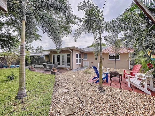 rear view of house featuring a sunroom, a yard, french doors, a fire pit, and a patio area