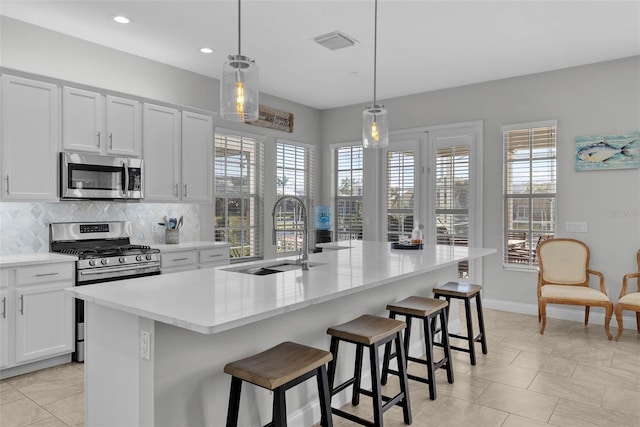 kitchen featuring sink, hanging light fixtures, a center island with sink, stainless steel appliances, and a kitchen bar