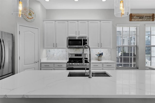 kitchen with hanging light fixtures, white cabinetry, appliances with stainless steel finishes, and light stone counters