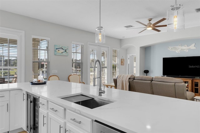 kitchen with light stone counters, beverage cooler, sink, and hanging light fixtures