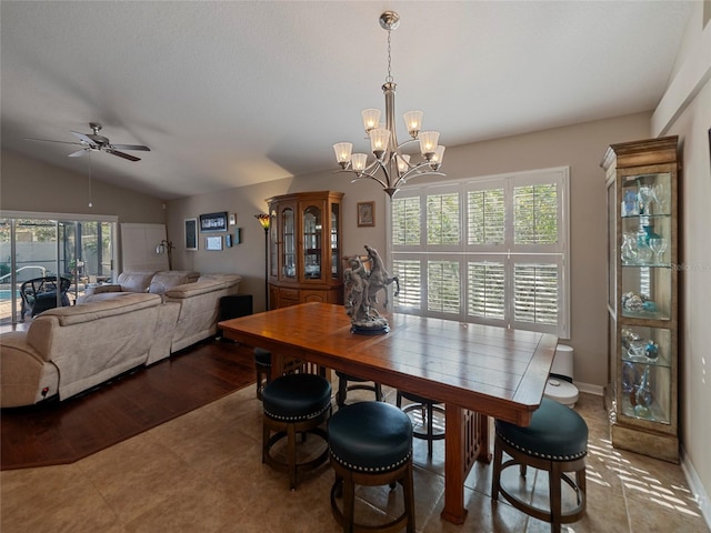 tiled dining room with ceiling fan with notable chandelier, vaulted ceiling, and a healthy amount of sunlight