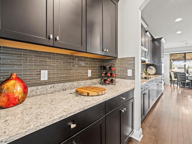 kitchen with light stone counters, dark hardwood / wood-style flooring, black cooktop, a textured ceiling, and decorative backsplash