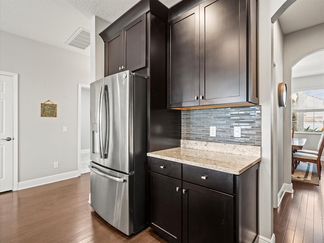 kitchen featuring stainless steel refrigerator with ice dispenser, tasteful backsplash, light stone counters, a textured ceiling, and dark wood-type flooring