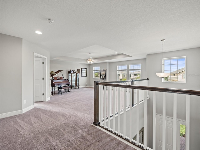 corridor with a tray ceiling, light carpet, plenty of natural light, and a textured ceiling