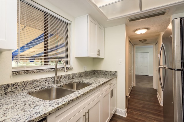 kitchen with dark wood-type flooring, white cabinets, sink, stainless steel fridge, and light stone countertops