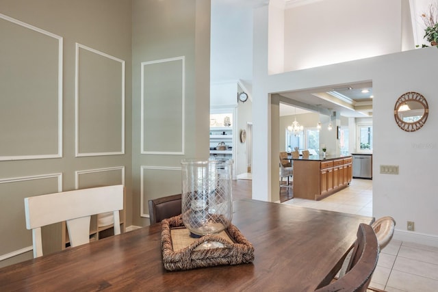 tiled dining room with a tray ceiling, crown molding, a high ceiling, and a chandelier