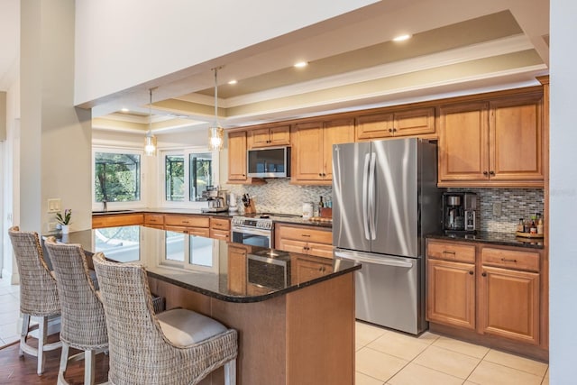 kitchen with dark stone countertops, appliances with stainless steel finishes, pendant lighting, a kitchen island, and ornamental molding