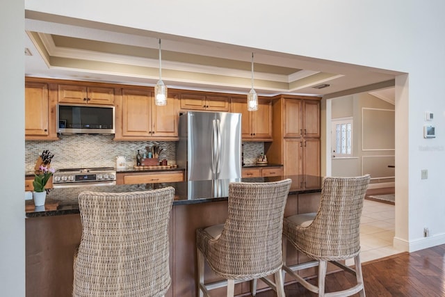 kitchen with light wood-type flooring, decorative light fixtures, a tray ceiling, appliances with stainless steel finishes, and ornamental molding