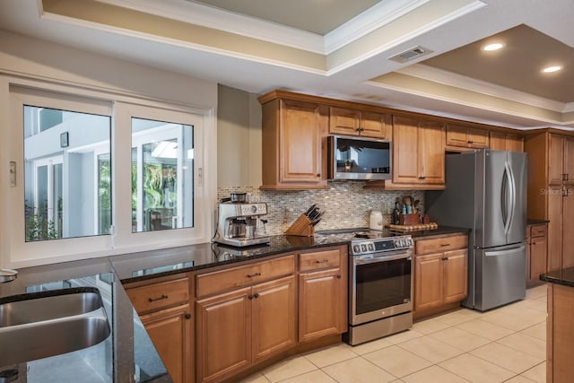 kitchen featuring backsplash, stainless steel appliances, a tray ceiling, and dark stone countertops