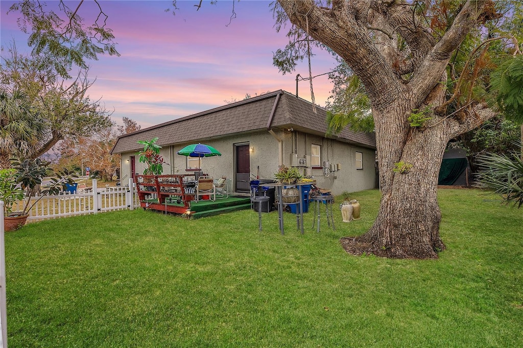 back house at dusk featuring a wooden deck and a yard