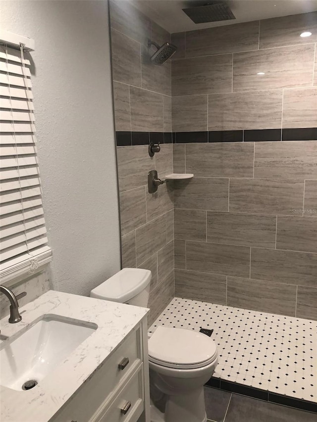 bathroom with a tile shower, vanity, and toilet